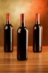 Three bottles of red wine on wooden table and golden background