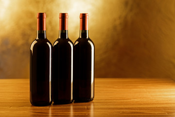 Fototapeta na wymiar Three bottles of red wine on wooden table and golden background