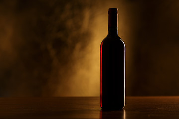 Fototapeta na wymiar Red wine bottle on wooden table and dark background - silhouette