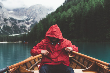 Man with red raincoat rowing a wood boat on Braies lake	
