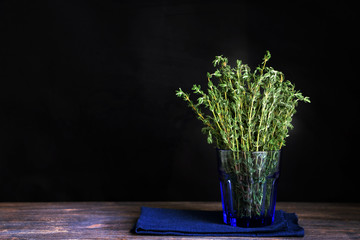 Fresh green thyme against black background with blue tissue and in blue glass. Special light, sekective focus.
