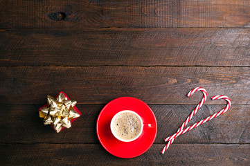 Coffee cup, candy canes and christmas present on dark wooden background. Gift box for holidays. Christmas background. Top view. Copy space