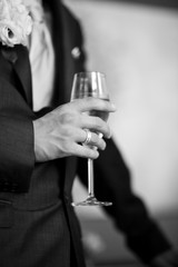 Black and white photo of champagne flute held by groom in tuxedo