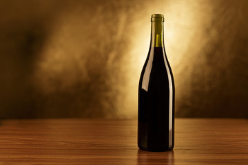 Fototapeta na wymiar Red wine bottle on wooden table and golden background