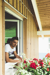 Young man at the window in a wood house with plants - 122625341