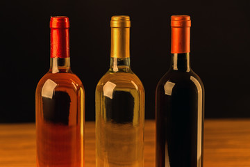 Rose, white and red wine bottles on wooden table and black background