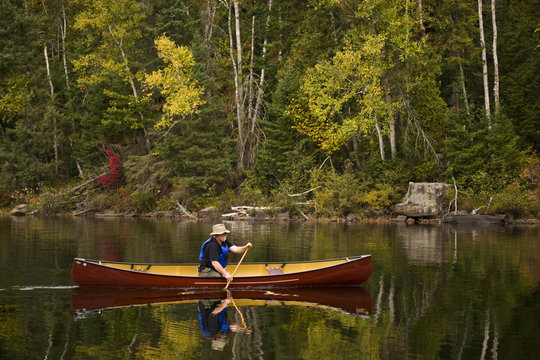 Elderly man canoeing  on Oxtongue Lake in autumn, Mukoka, Ontario, Canada.