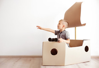 Little boy playing with cardboard ship on white wall background