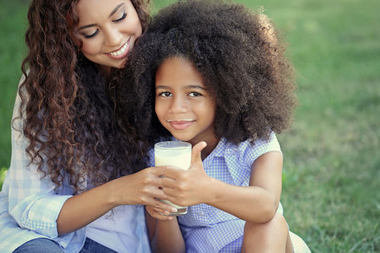 African-American woman and her daughter drinking milk and sitting on the lawn