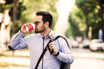 Young businessman walking outside and drinking coffee.