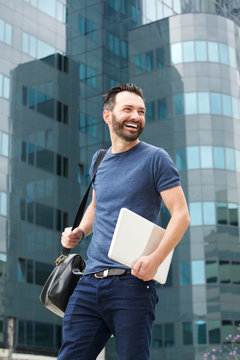 Smiling Businessman Walking Outdoors With Handbag And Laptop