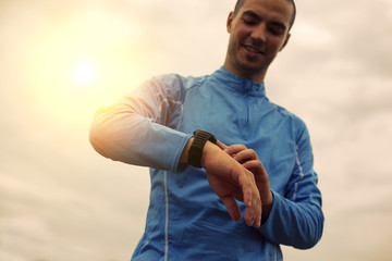 Happy athlete is looking at smart watch, sunlight effect