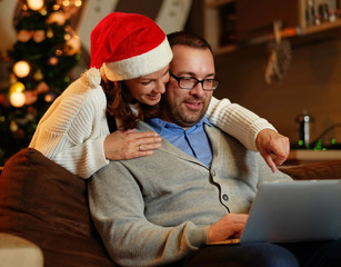 Smiling female and plump male using laptop on christmas.