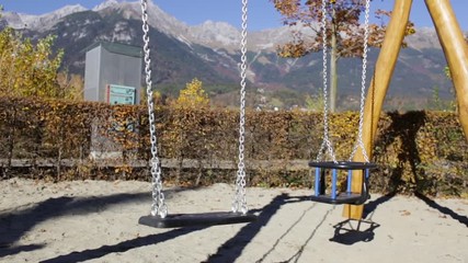 Empty swing moving with the wind at the playground with mountains in the background