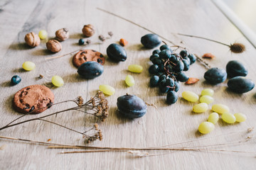 lying on wooden background grapes, plums, dry grass,seeds, thist