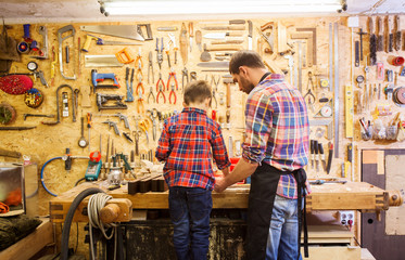 father and little son with wood plank at workshop - obrazy, fototapety, plakaty