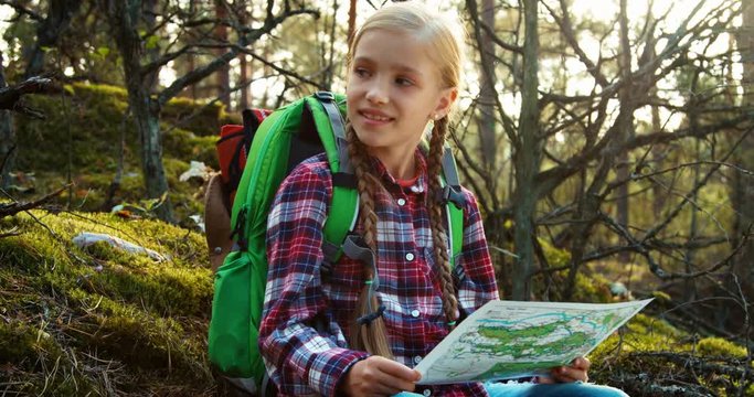 Young hiker girl using her map and sitting in the forest