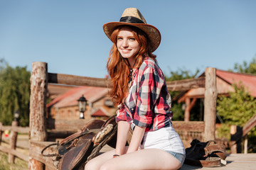 Cute redhead cowgirl sitting and resting on the ranch fence