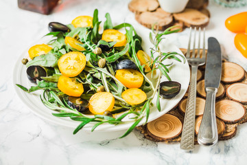 fresh green salad with arugula, yellow tomatoes, olives, grapes