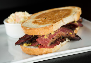 Smoked meat beef sandwich with custard and black pepper corns, served on a plate with coleslaw.