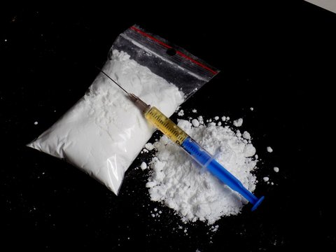 Injection syringe on cocaine drug powder pile and cocaine bag on black background