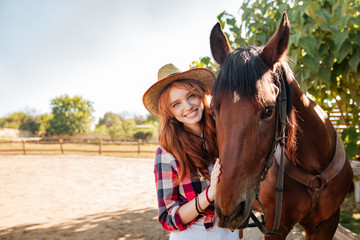 Fototapeta premium Smiling pretty young woman cowgirl in hat with her horse