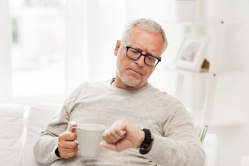 senior man with coffee looking at wristwatch
