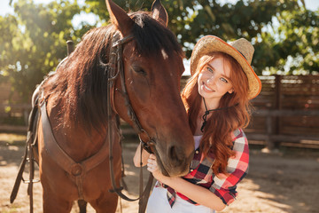 Smiling pretty young woman cowgirl in hat with her horse