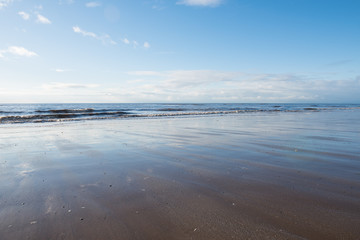 relaxing and gentle calming waves flowing into a beach at sundown, with a vivid blue sky and reflection