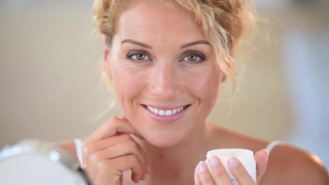 Middle-aged blond woman putting cosmetics on