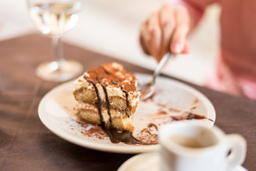 Young woman eating homemade traditional dessert tiramisu with coffee and glass of wine