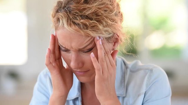 Woman with migraine putting eyeglasses on