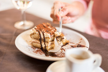 Young woman eating homemade traditional dessert tiramisu with coffee and glass of wine