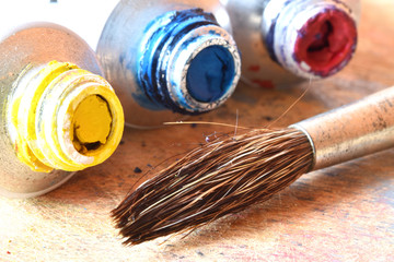 A paint brush near three little tubes (yellow, red, blue)