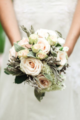 A cute wedding bouquet in gentle female hands, white dress background