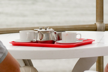 Teapot and cups on red plastic tray on table at seaside cafe