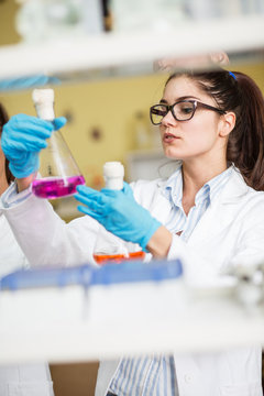 Young female scientist in lab coat wearing gloves, doing experiments in lab.