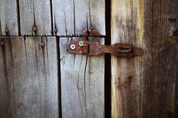 Old rusty lock hanging on the gray wooden door.