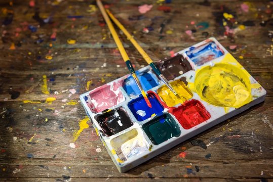 Colorful colors palette and paint brushes on dirty wooden artist table