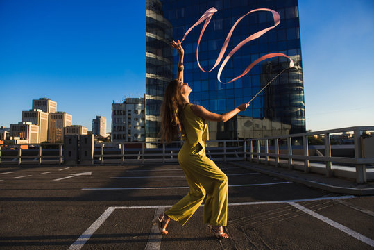 Gymnast girl with ribbon. Professional gymnast woman dancer posing with ribbon on the roof of the building. The skyscraper in the background.