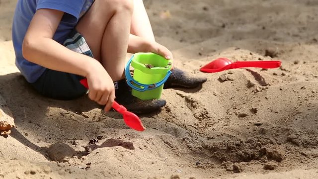 A boy plays in the sandbox with shovel and pail and shapes for sand
