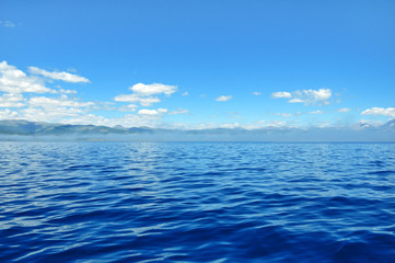 Obraz premium sea lanscape. blue sky, clouds over the surface of sea. mountain on horizon