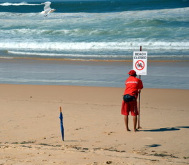 A sign reads beach closed. No swimming flag on the beach before/after storm.