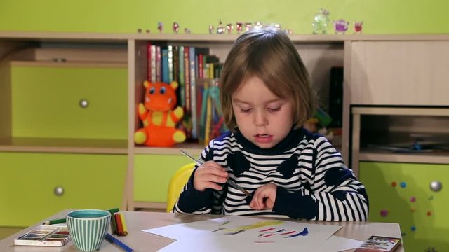 Little girl draws something using brush and pencil, tries to watching TV.