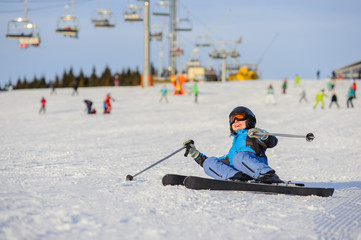 Young happy girl skier in blue ski suit after the fall on mountain slope. Ski resort. Winter sports concept.