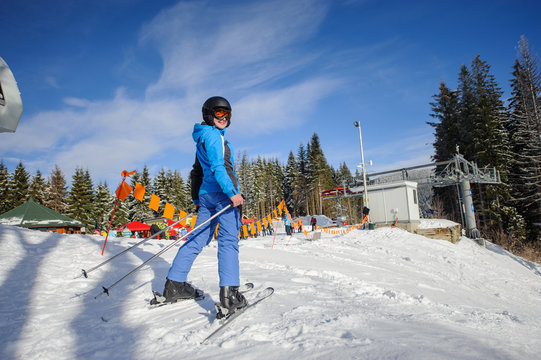 Female skier on the top of ski slope on a sunny day at ski resort. Woman is smiling and looking at the camera. Carpathian mountains.