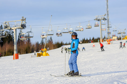 Portrait of active happy woman skier at the ski resort on a sunny day against ski-lift. Girl is wearing blue jacket helmet and goggles and looking to the camera. Carpathian Mountains