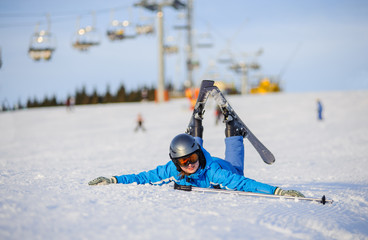 Fototapeta na wymiar Young tired skier woman in blue ski suit orange goggles and helmet lying on the snow on a sunny day against ski-lift at ski resort. Winter vacation.