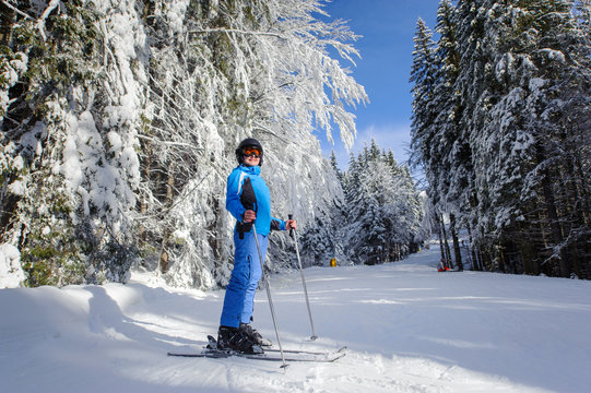Young female skier on a ski slope in the forest with big beautiful trees covered in snow. Winter sports concept. Wide angle. Carpathian Mountains, Bukovel, Ukraine