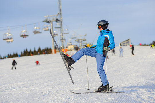 Full length portrait of female skier standing with one raised leg on a ski slope at a sunny day against ski-lift. Winter vacation. Ski resort at Carpathian Mountains, Bukovel, Ukraine